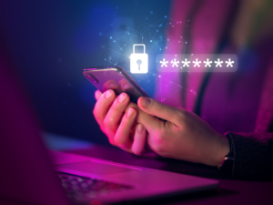 cyber essentials update Image of hands holding phone, by laptop, with a graphic of a padlock and stars indicating a password